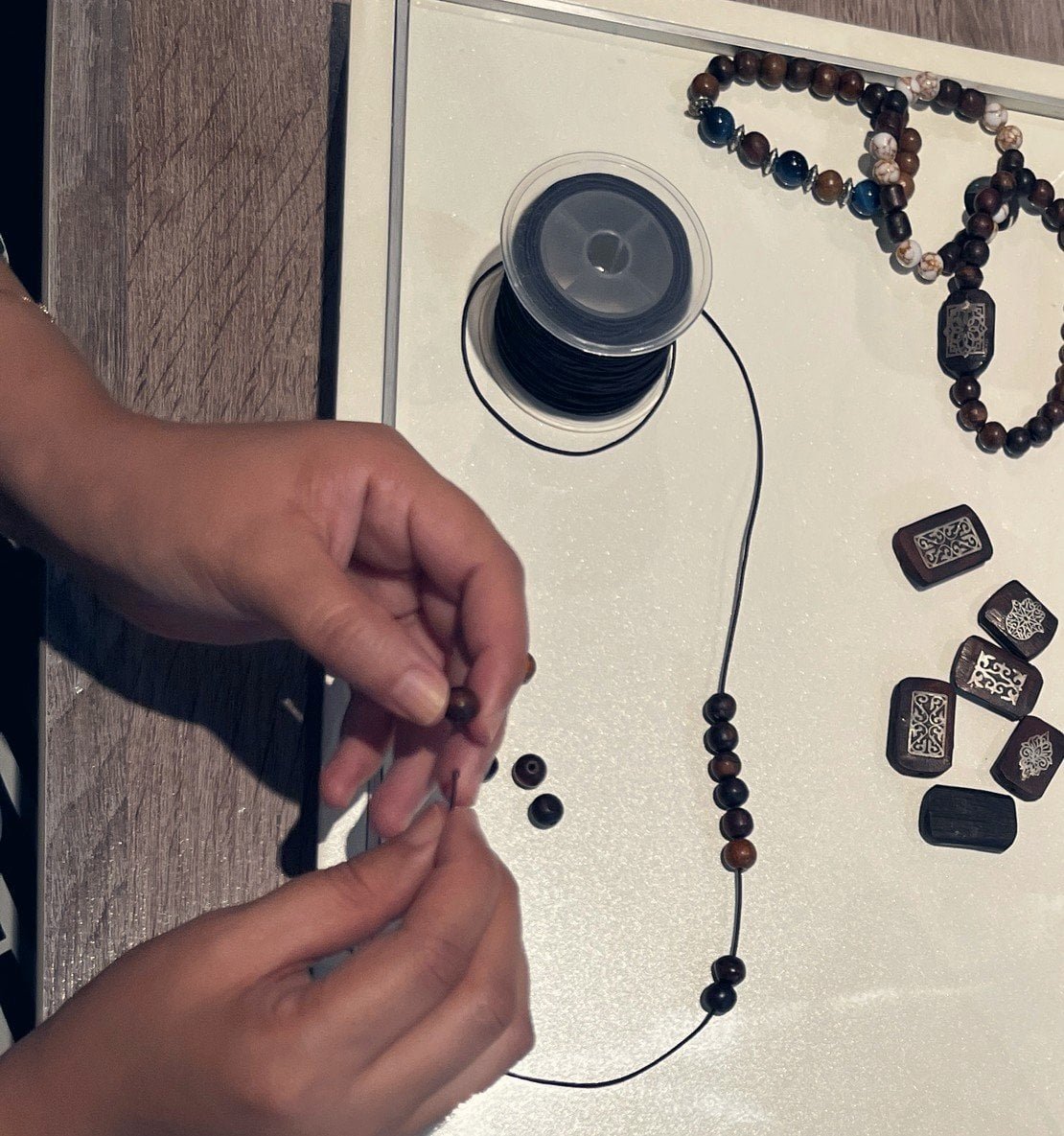 Mains de l'artisane enfilant des perles d'oud dans l'atelier Soltan Al Oud, Kénitra